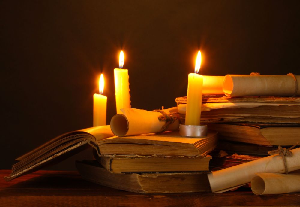 19510605 - pile of old books with candle and scroll in dark